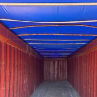 An empty shipping container with red walls and a blue tarp ceiling, creating a spacious interior.