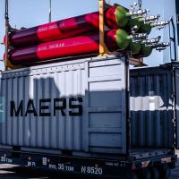 Cargo container with red and green gas cylinders, a ladder and port machinery in the background.