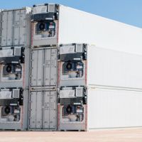 Stacked refrigerated containers against a clear blue sky, with one white container in the foreground.