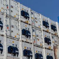 Refrigerated shipping containers stacked, featuring blue cooling units against a bright blue sky.